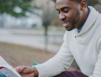 Young black man sitting on a park bench reading a book