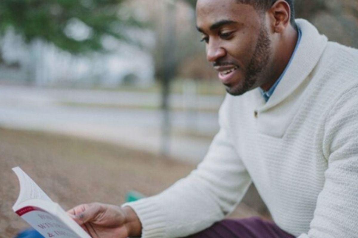 Young black man sitting on a park bench reading a book